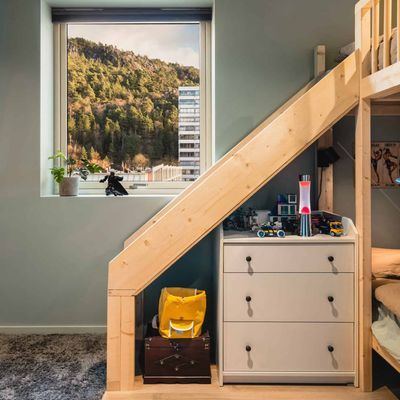 Barnerom med utsikt til boligblokk og skog, sengetrapp og hvit kommode