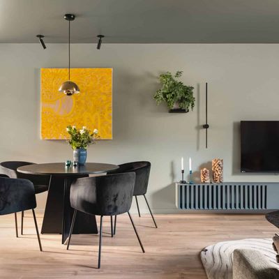 Stue med spisebord, sorte stoler, gul kunstplakat og veggmontert TV