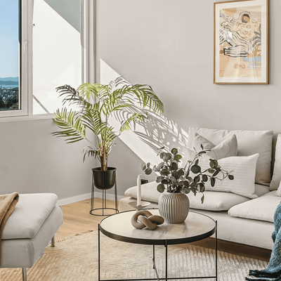 Hjørnestue med hvit sofa, palme og bilde på lys vegg