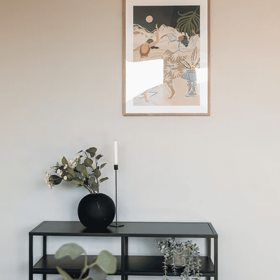 Detalj av konsollbord med plante, lysestake og innrammet plakat