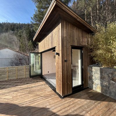 Hjørnet av annekset med stående trekledning, glassdør og natursteinsmur