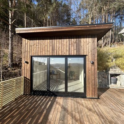 Anneks med lukkede skyvedører i glass og utstikkende takutspring mot terrassen
