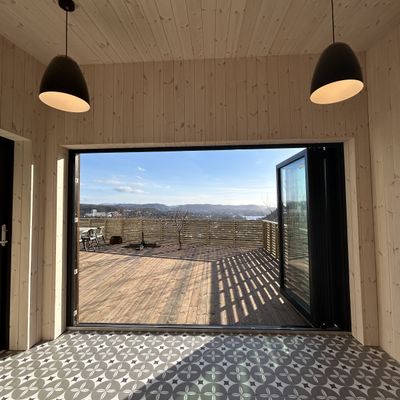 Utsyn fra annekset gjennom åpne skyvedører mot terrasse og Bergen i det fjerne
