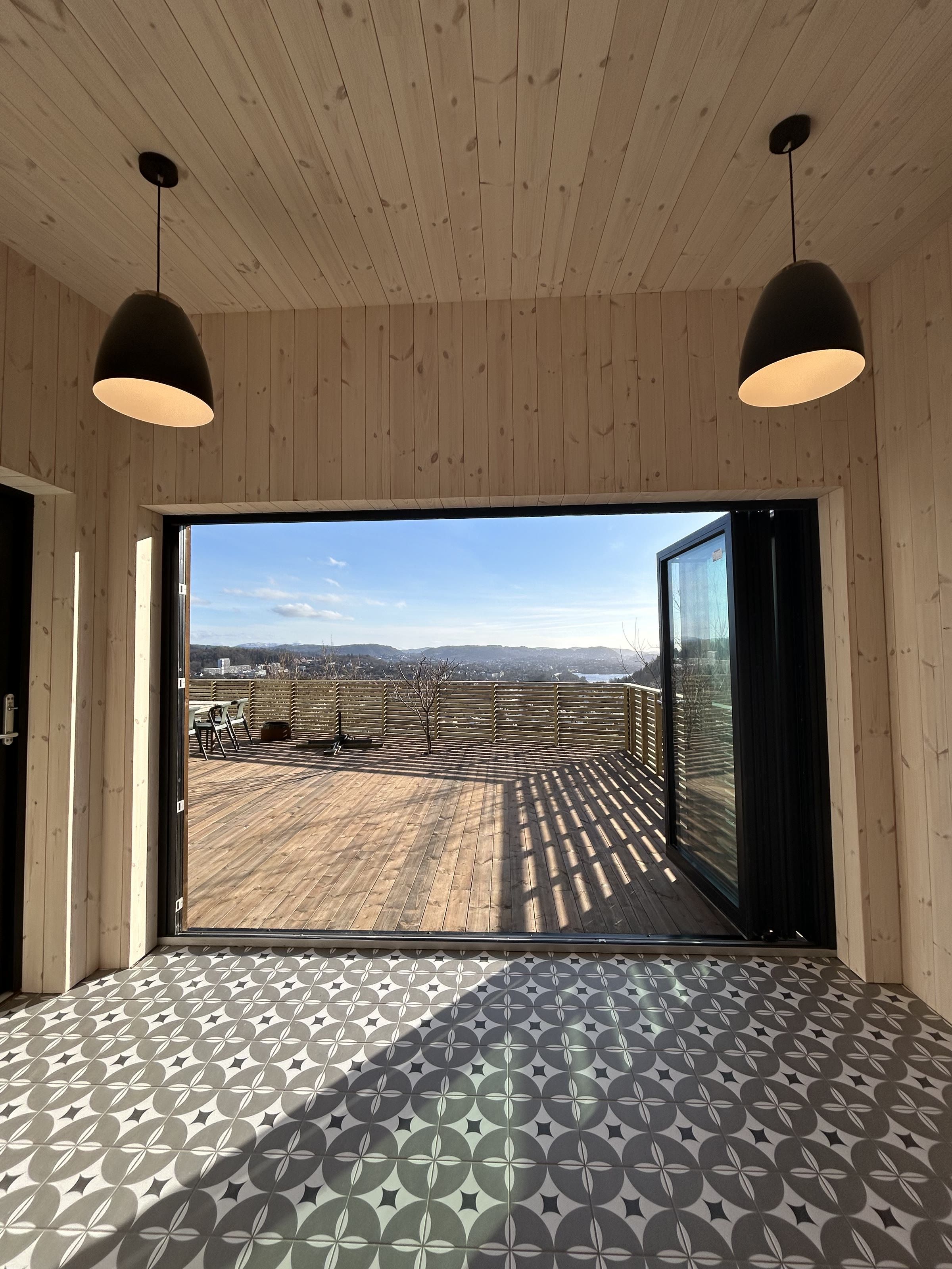 Utsyn fra annekset gjennom åpne skyvedører mot terrasse og Bergen i det fjerne