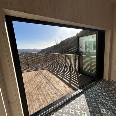Vindusåpning i annekset med sort karm og skyggespill fra spileveggen på terrassen
