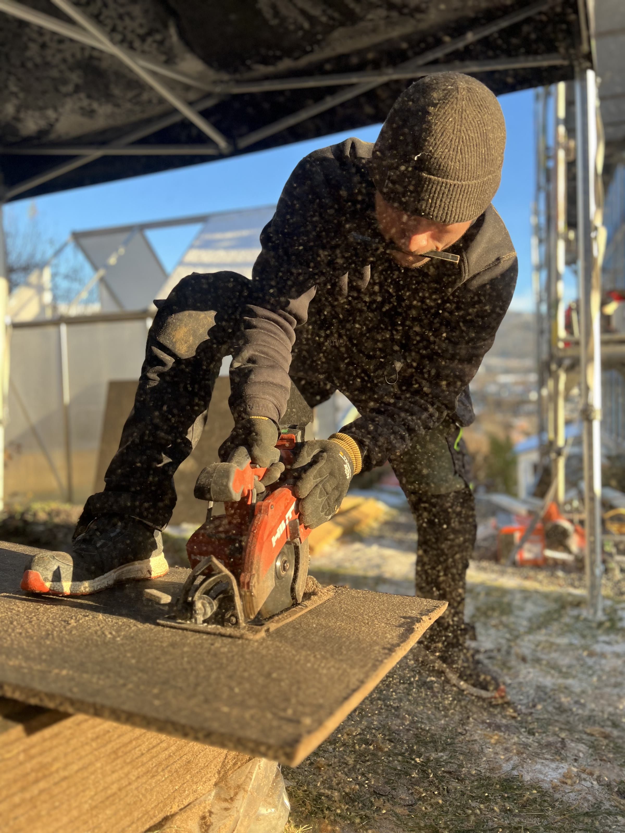 Håndverker som kapper betongplate med kappsag under presenning på en frostmorgen