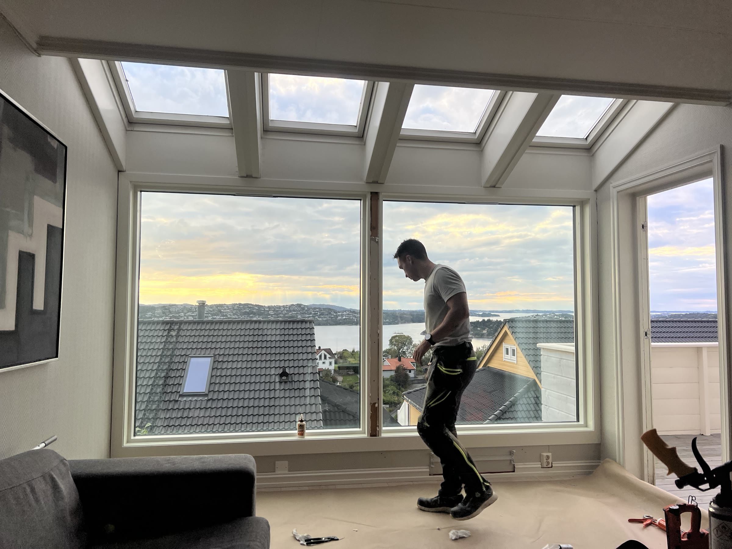 Håndverker som monterer store panoramavinduer i stue med utsikt over fjorden
