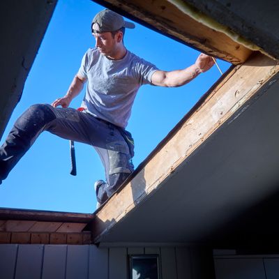 Håndverker som står bredbeint i den nye takåpningen med blå himmel bak seg