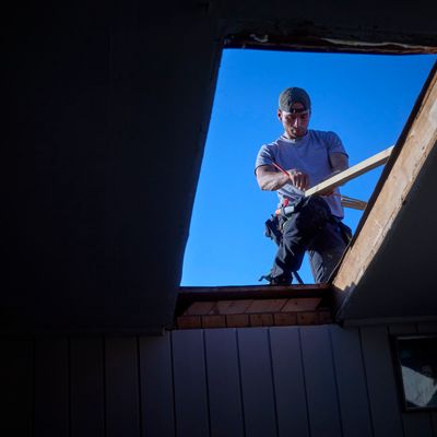 Håndverker som merker av en lekt med blyant, sett gjennom takåpningen fra det mørke loftet